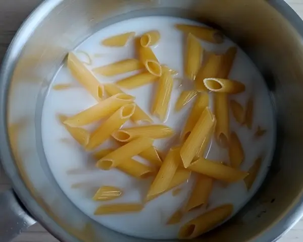 Makaron penne gotuje się w mleku w metalowym garnku.