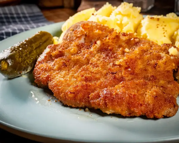Chrupiące kotlety z karkówki, purée ziemniaczane i ogórek kiszony na talerzu.
