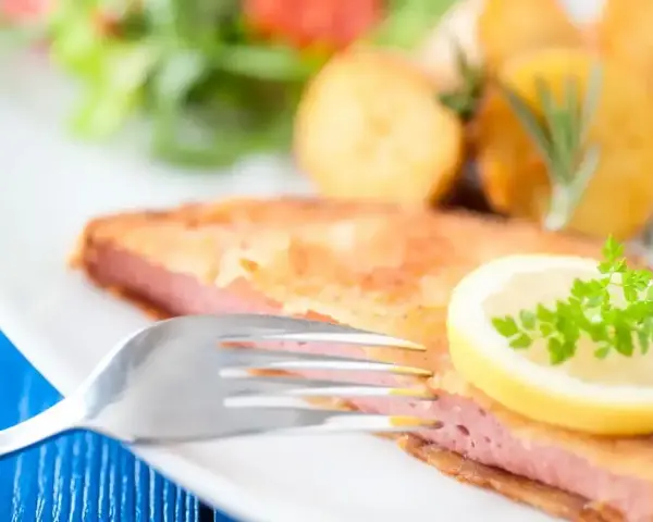 Smażony kotlet z mortadeli, podany z ziemniakami, sałatką i plasterkiem cytryny z natką pietruszki.