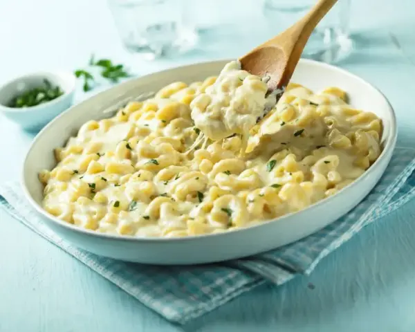 Kremowe makaronowe danie, idealne do przygotowania z przepisu na mac and cheese. Łyżka wydobywa porcję ciągnącego się sera.
