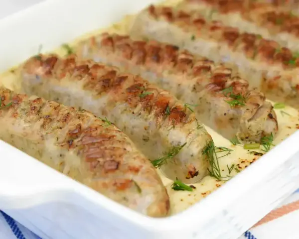 Pieczona biała kiełbasa w kremowym sosie chrzanowym, udekorowana świeżym koperkiem. Pyszne danie gotowe do podania.