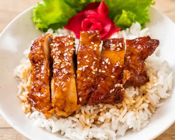 Pyszny kurczak w miodzie, polany sosem teriyaki i posypany sezamem, podany na ryżu z dodatkiem sałaty i marynowanego imbiru.