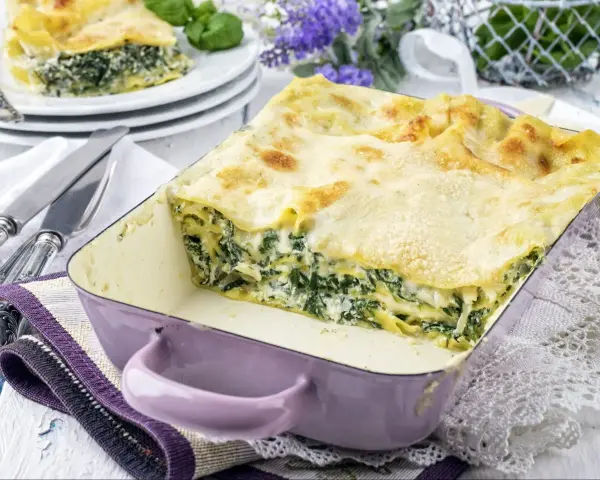 Pyszne lasagne ze szpinakiem i beszamelem, zapieczone na złoto, w fioletowym naczyniu. Idealna na rodzinny obiad.