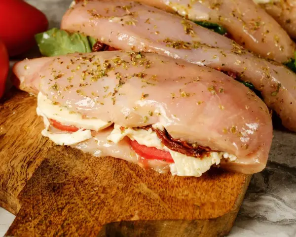 Nadziewana pierś z kurczaka z mozzarellą i suszonymi pomidorami, przyprawiona ziołami, gotowa do pieczenia.