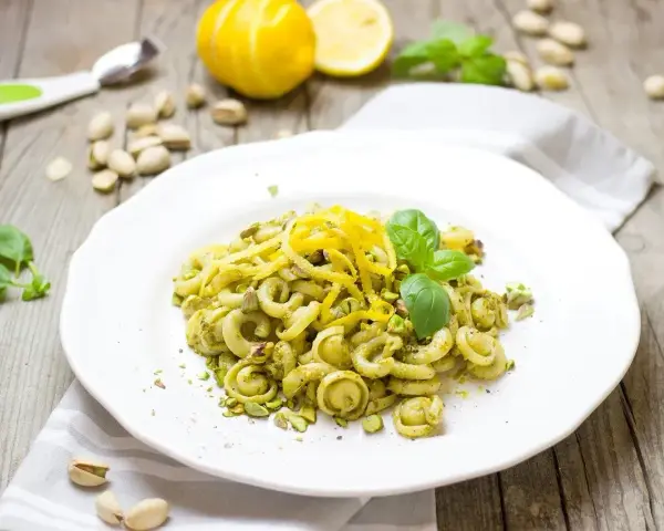 Makaron z zielonym pesto, którego głównym składnikiem są pistacje, ozdobiony skórką cytrynową i listkami bazylii.