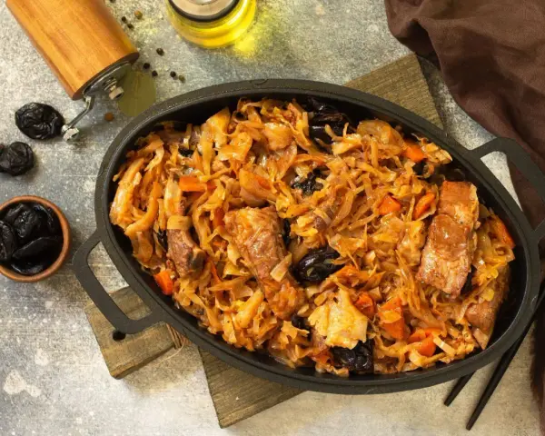 Pyszny bigos z kiszonej kapusty z kawałkami mięsa i śliwkami, podany w żeliwnym naczyniu.