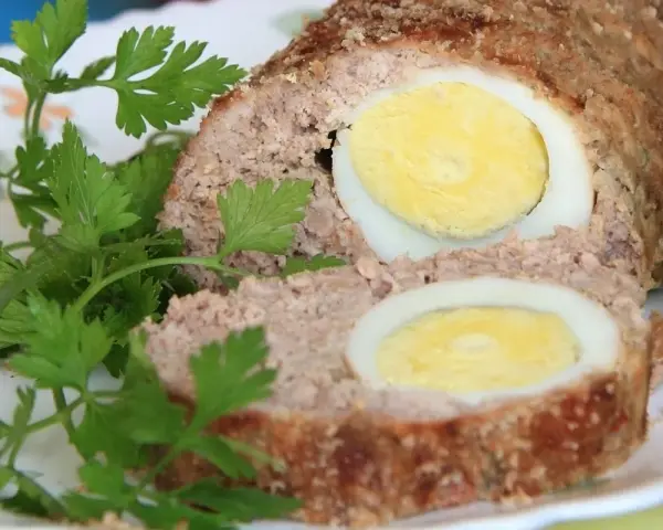 Pyszna pieczeń rzymska w sosie, z jajkiem w środku, udekorowana natką pietruszki.