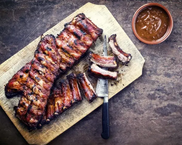 Soczyste żeberka w miodzie, grillowane do perfekcji, podane na desce z sosem.