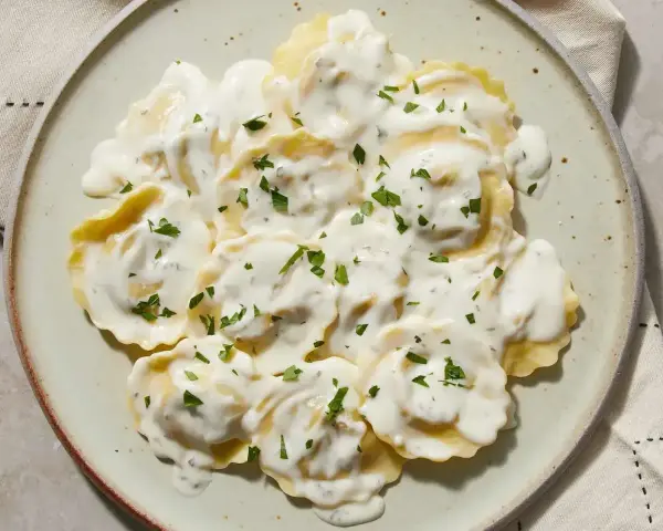 Ravioli w kremowym sosie, posypane natką pietruszki. Pyszny sos do ravioli, który zachwyca smakiem.