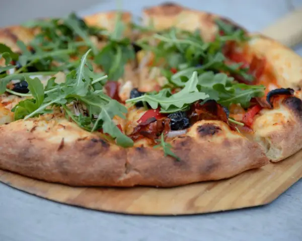 Pyszna pizza z rukolą i oliwkami na drewnianej desce. Proste ciasto na pizzę zawsze wychodzi, tworząc idealną bazę dla ulubionych dodatków.
