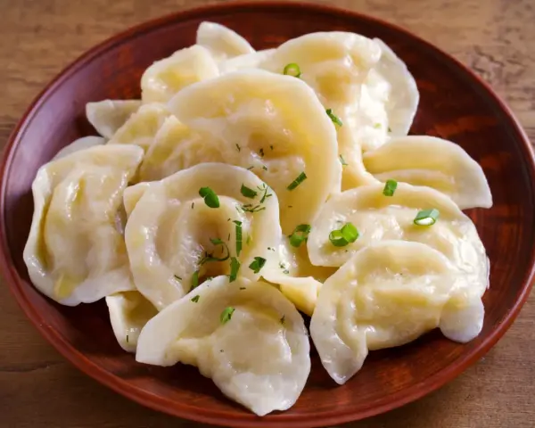 Pyszne pierogi z tradycyjnym farszem do uszek, posypane szczypiorkiem, na glinianym talerzu.