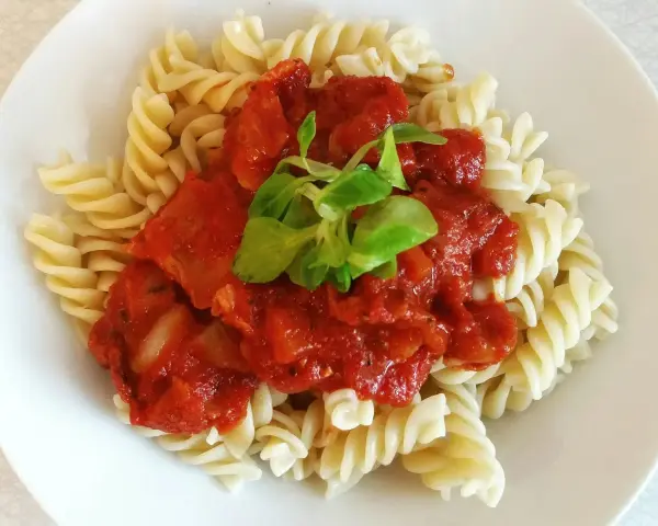 Fusilli z sosem pomidorowym i pomidorkami koktajlowymi, udekorowane świeżą zieleniną. Pyszne danie gotowe w kilka minut.