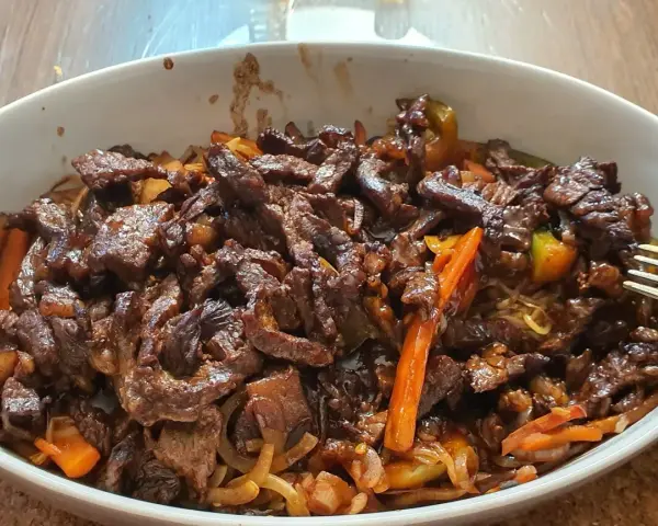 Pyszne wołowina stir fry z warzywami i makaronem, podane w białej misce.
