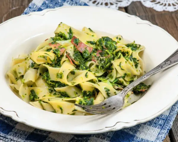 Pappardelle z boczkiem i szpinakiem, danie pełne smaku, podane na talerzu z widelcem.