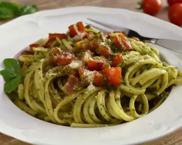 Pyszny makaron z pesto, pomidorkami i parmezanem, udekorowany listkiem bazylii. Idealny na szybki obiad.