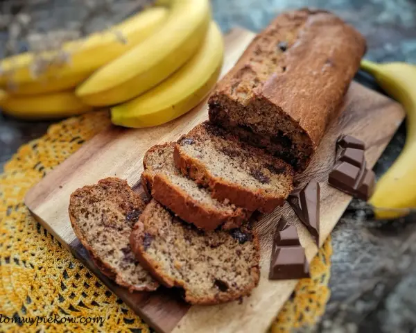 Pyszny chlebek bananowy z czekoladą, pokrojony na kromki, obok świeże banany i kawałki czekolady.
