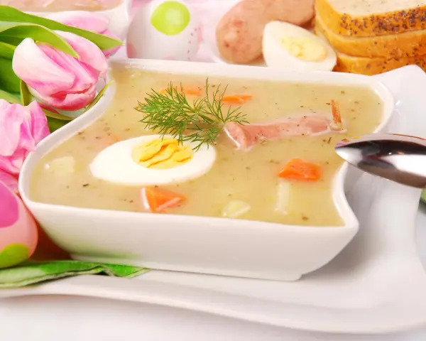 Biały barszcz z jajkiem, kiełbasą, marchewką i koprem, ozdobiony tulipanami i pisankami.