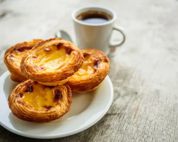 Na talerzyku leżą trzy chrupiące pastéis de nata, obok filiżanka kawy. Idealny poranek.