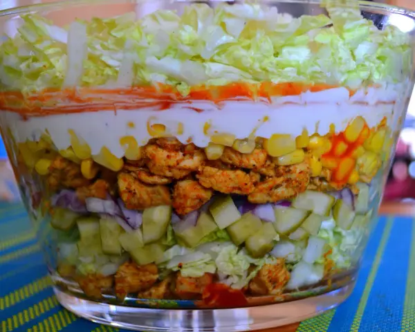Warstwowa sałatka z kurczakiem w stylu gyros, z kukurydzą, ogórkiem, cebulą i sosem.