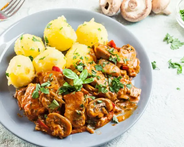 Gulasz drobiowy z pieczarkami i ziemniakami na talerzu, ozdobiony natką pietruszki.