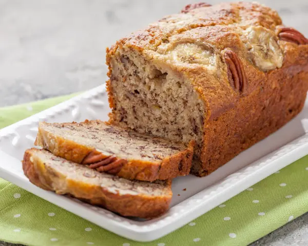 Wilgotny chlebek bananowy z olejem, udekorowany orzechami pekan i plasterkami banana. Idealny na podwieczorek.