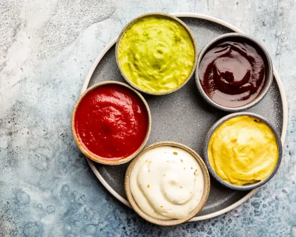 Sześć miseczek z sosami: zielony guacamole, czerwony ketchup, ciemny barbecue, żółta musztarda i biały majonez. Idealne do dań, gdy zastanawiasz się, jak zrobić sos.
