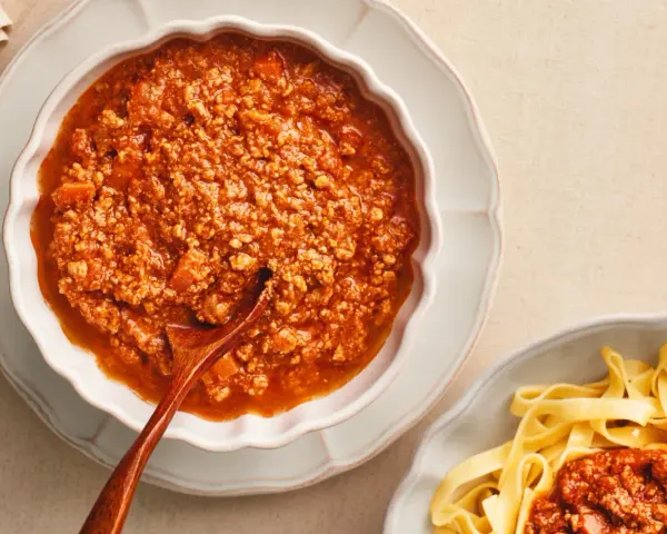 Gęsty, aromatyczny sos do spaghetti bolognese w miseczce, obok porcji makaronu tagliatelle.
