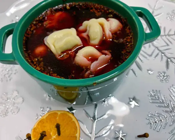 Aromaticzny barszcz z uszkami w zielonej miseczce, ozdobiony suszoną pomarańczą i goździkami.