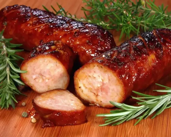 Soczysta kiełbasa pieczona w piekarniku, skropiona błyszczącym sosem, z gałązkami rozmarynu i ziarnami pieprzu.