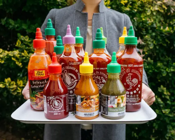 Taca z wieloma butelkami sosu Sriracha o różnych kolorach nakrętek.