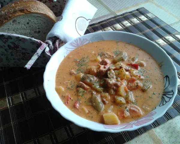 Pyszny bogracz z pieczarkami, ziemniakami i mięsem, posypany natką. Obok koszyk z chlebem.