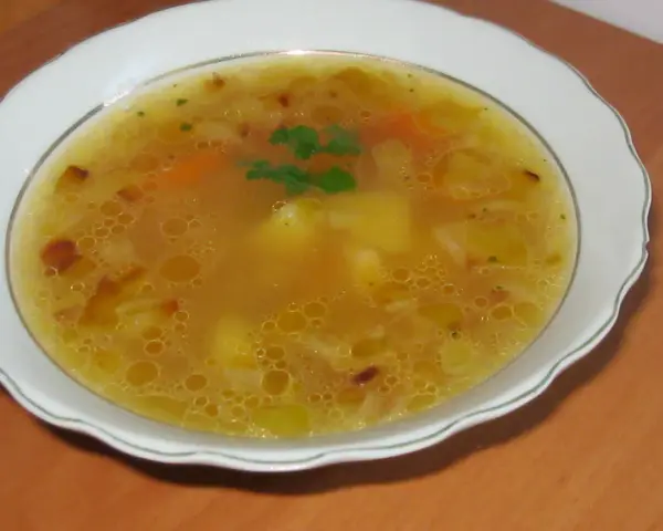 Prosta zupa cebulowa z ziemniakami, z kawałkami marchewki i natką pietruszki, podana w białej misce.