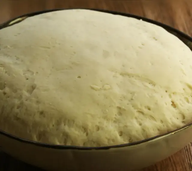 Puszyste ciasto na pizzę wyrosło w misce, gotowe do dalszej obróbki.