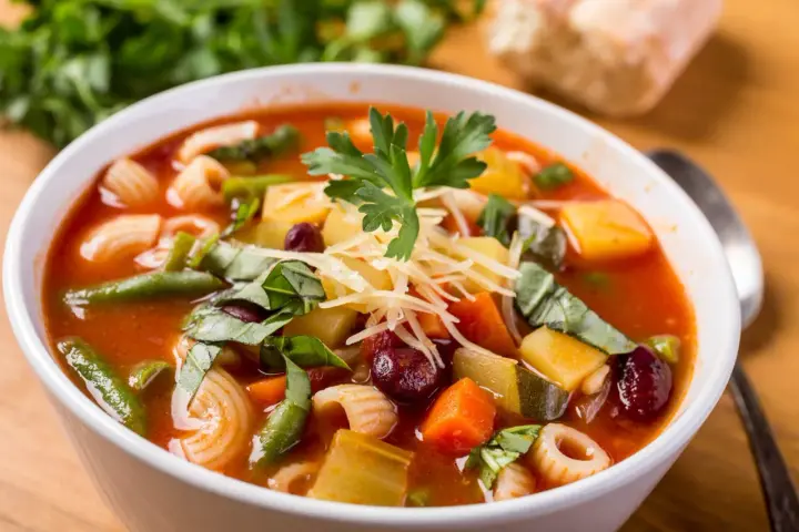 A miseczce aromatyczna zupa minestrone, oryginalny przepis z makaronem, fasolką, ziemniakami i startym parmezanem.