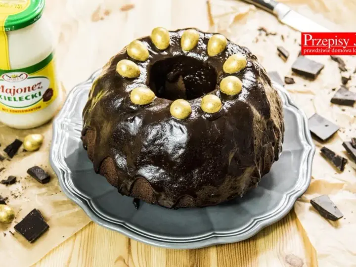 Babka majonezowa z przepisów Joli, polana czekoladą i ozdobiona złotymi jajeczkami. Obok słoik majonezu i kawałki czekolady.