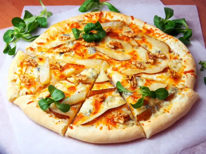 Apetyczna pizza z gruszką i gorgonzolą, ozdobiona orzechami włoskimi i świeżą rukolą. Idealna na wyjątkowy wieczór.