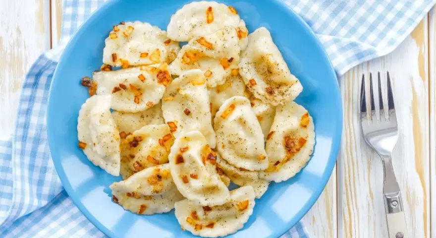 Pyszne pierogi z soczewicą czerwoną, posypane skwarkami i pieprzem, na niebieskim talerzu.