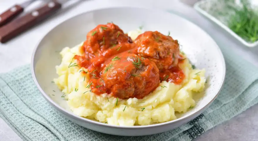 Pyszne pulpeciki w sosie pomidorowym na kremowym purée ziemniaczanym, posypane świeżym koperkiem.