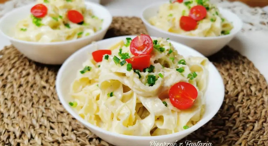 Pyszny makaron tagliatelle w kremowym sosie 4 sery, udekorowany pomidorkami koktajlowymi i szczypiorkiem. Idealny na szybki obiad.