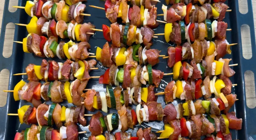 Szaszłyki w piekarniku gotowe do pieczenia: mięso, papryka, cebula i cukinia na patyczkach.