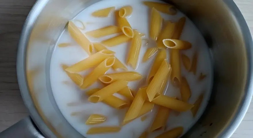 Makaron penne gotuje się w mleku w metalowym garnku.