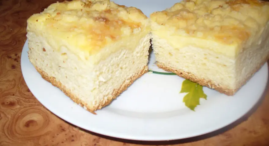 Dwa kawałki puszystego ciasta drożdżowego z kremowym nadzieniem i kruszonką, gotowe do pieca.