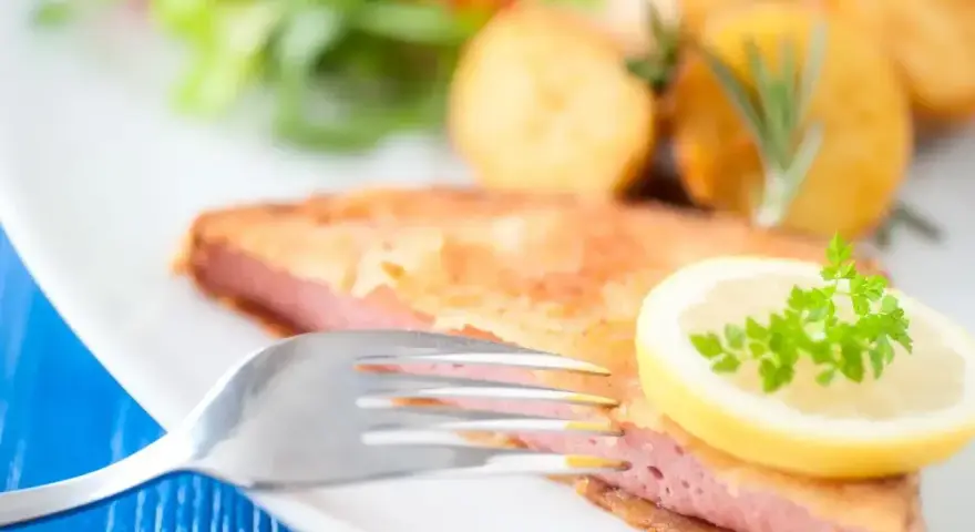 Smażony kotlet z mortadeli, podany z ziemniakami, sałatką i plasterkiem cytryny z natką pietruszki.