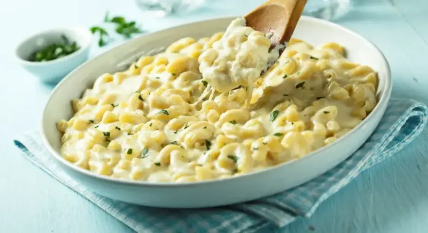 Kremowe makaronowe danie, idealne do przygotowania z przepisu na mac and cheese. Łyżka wydobywa porcję ciągnącego się sera.