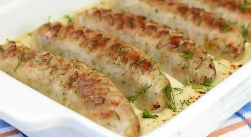 Pieczona biała kiełbasa w kremowym sosie chrzanowym, udekorowana świeżym koperkiem. Pyszne danie gotowe do podania.