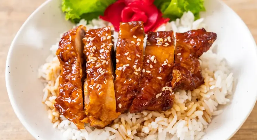 Pyszny kurczak w miodzie, polany sosem teriyaki i posypany sezamem, podany na ryżu z dodatkiem sałaty i marynowanego imbiru.