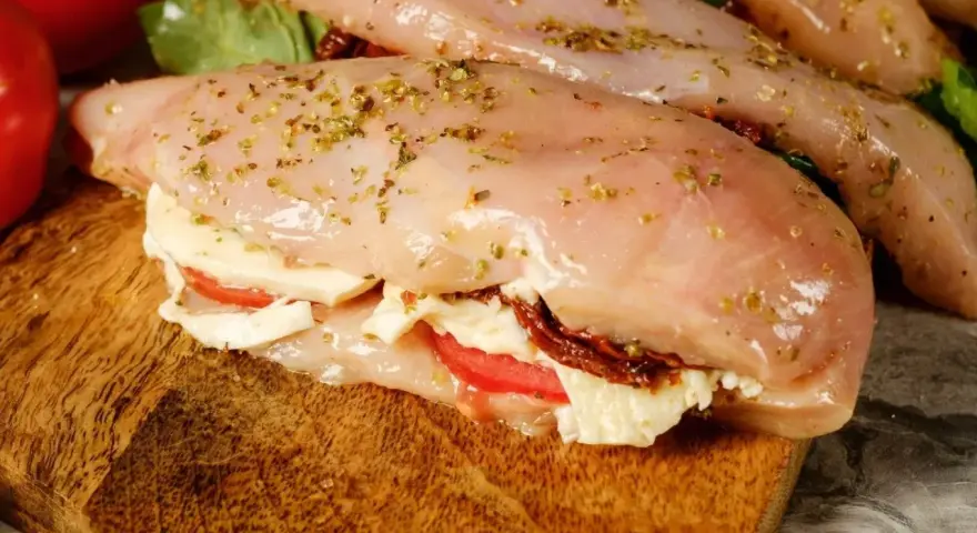 Nadziewana pierś z kurczaka z mozzarellą i suszonymi pomidorami, przyprawiona ziołami, gotowa do pieczenia.