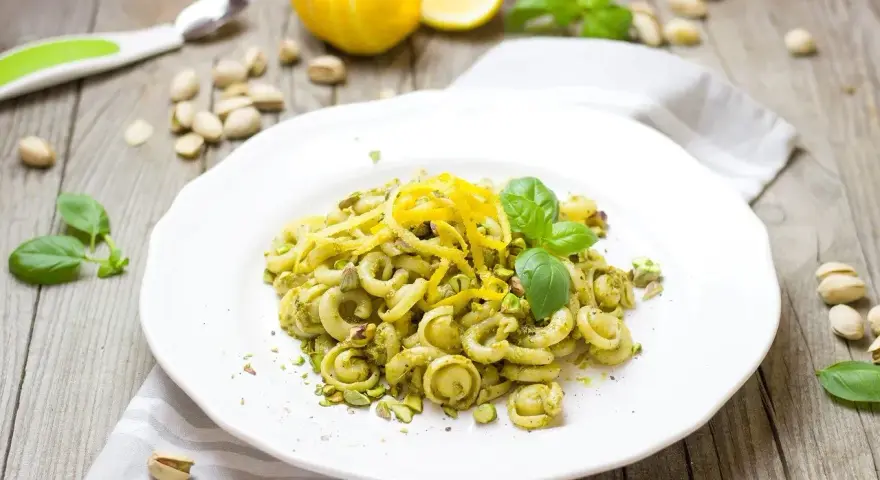 Makaron z zielonym pesto, którego głównym składnikiem są pistacje, ozdobiony skórką cytrynową i listkami bazylii.
