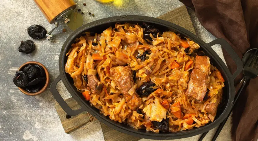 Pyszny bigos z kiszonej kapusty z kawałkami mięsa i śliwkami, podany w żeliwnym naczyniu.