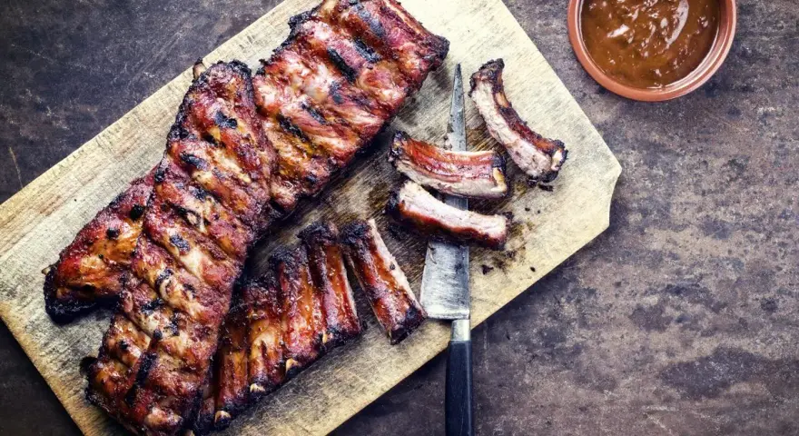 Soczyste żeberka w miodzie, grillowane do perfekcji, podane na desce z sosem.